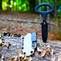 
              Ulticlip 2.2 on a knife sheath on a log beside a dagger. 
            
